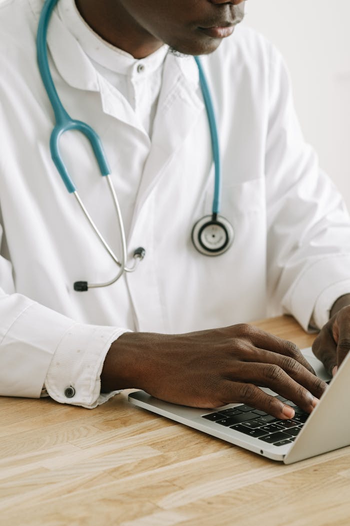 services-03 A professional doctor in a white coat with stethoscope typing on a laptop in an office setting.
